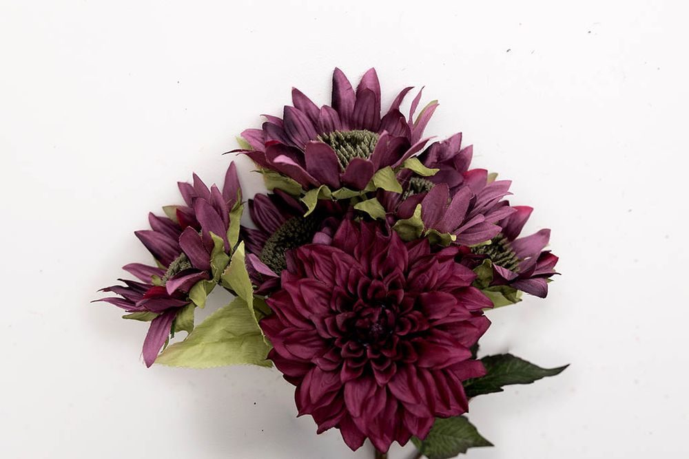 Deep purple artificial dahlia bouquet with multiple blooms and green leaves on white background.