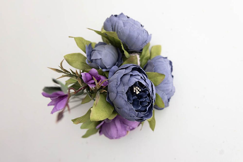 Artificial blue and purple peony bouquet with green foliage on white background.