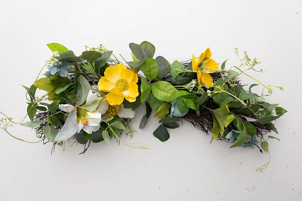 Decorative floral swag with yellow and white flowers and green foliage on white background.