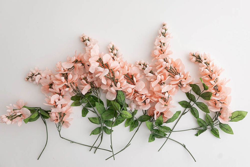 Delicate pink artificial larkspur flower stems with green leaves arranged on a white background.