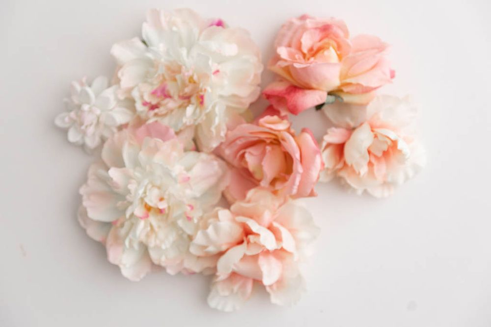 Soft pink and white artificial peony flower heads scattered on a clean white surface.