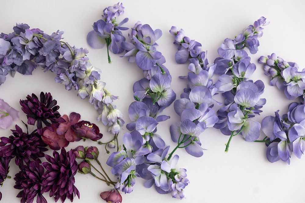 Purple artificial wisteria stems and dark burgundy chrysanthemum flowers arranged on white background.