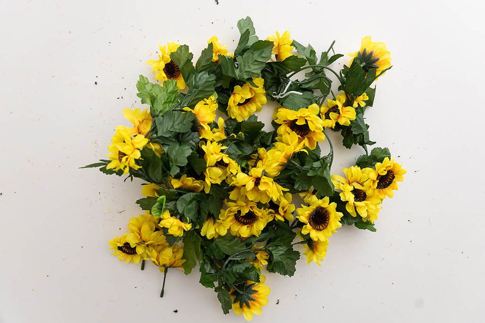 Bright yellow artificial sunflowers with green leaves clustered together on a white background.