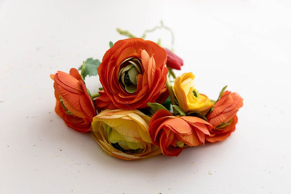 Vibrant orange and yellow artificial ranunculus flowers grouped together on a white surface.