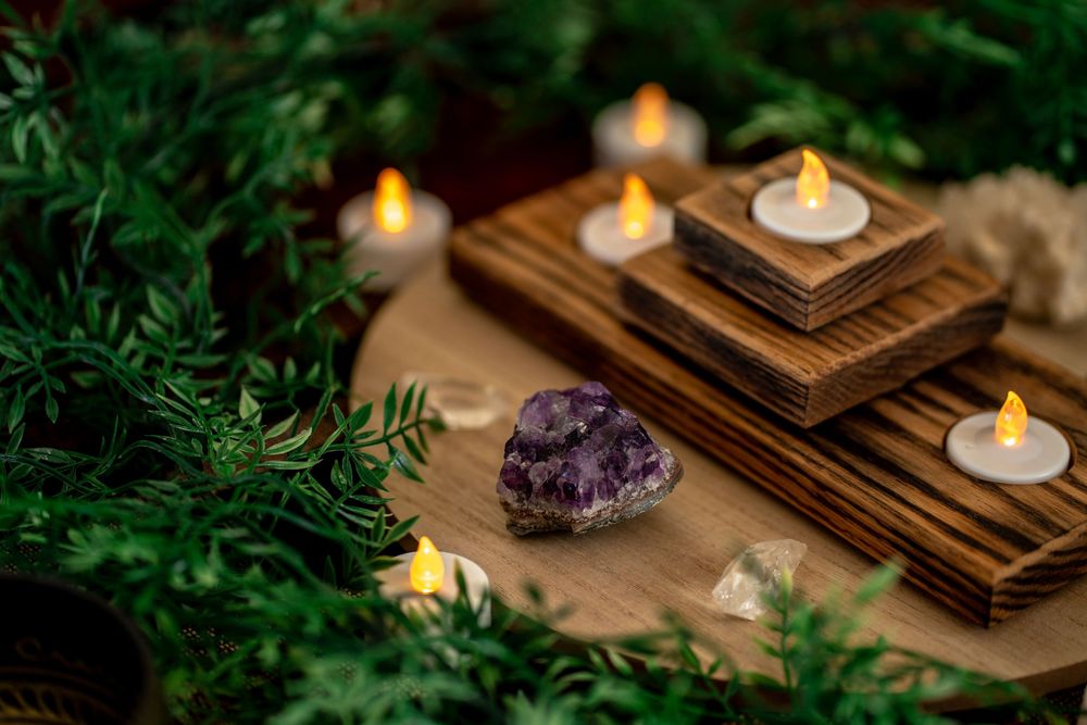 Amethyst crystal and LED tea light candles on wooden holders surrounded by lush green foliage. Carlsbad, CA