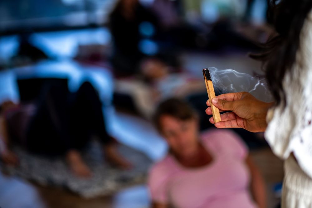 Hand holding burning incense stick with smoke rising during a group meditation or yoga session indoors. Carlsbad, CA