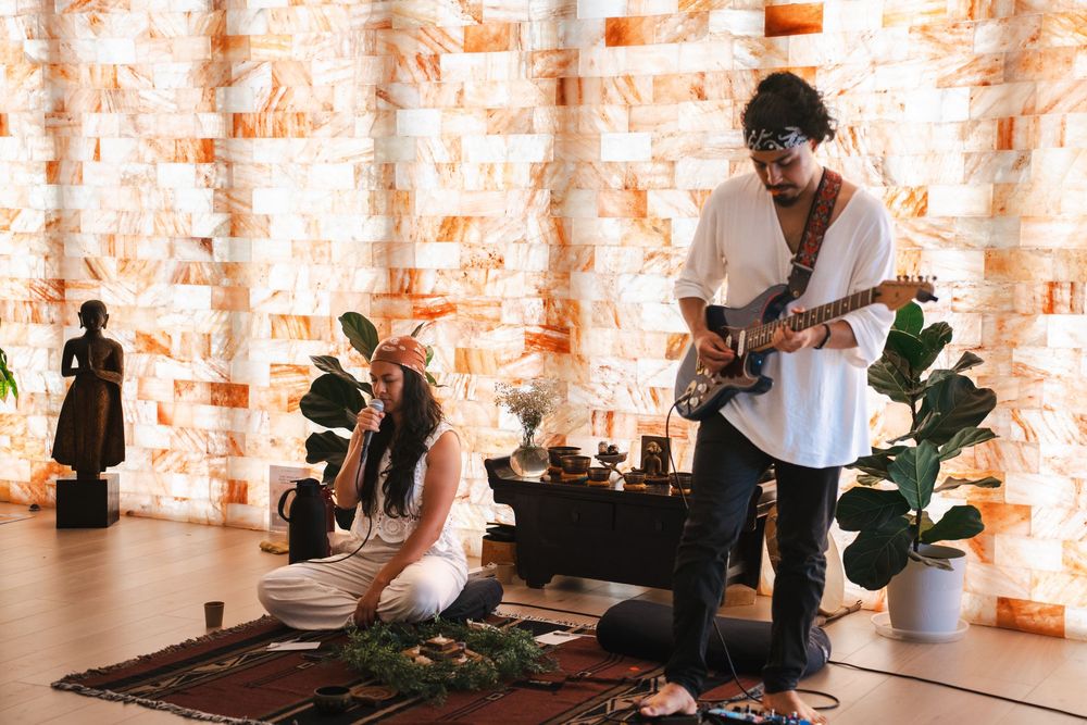 A musician plays guitar during a sound healing session in a salt cave with singing bowls and plants. Vista, CA