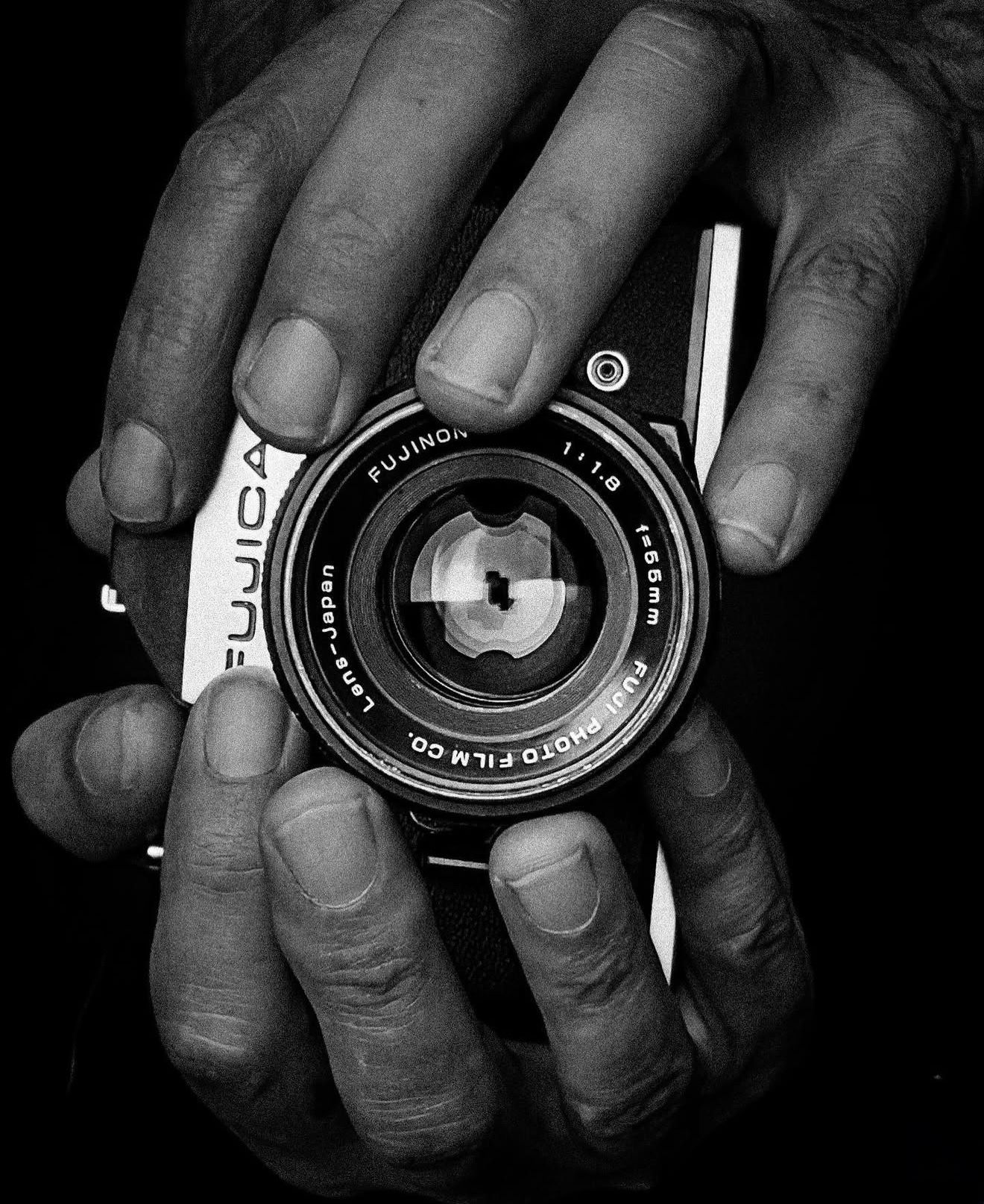 Close-up black and white photo of hands holding a vintage Fujica camera with a Fujinon 45mm f/1.8 lens.