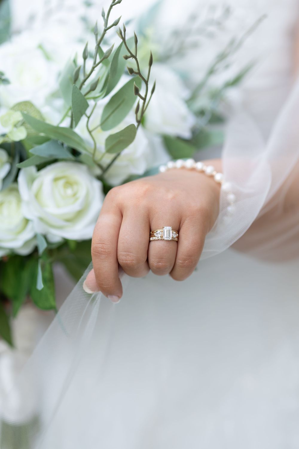 Close-up of bride's hand wearing a diamond engagement ring with pearl bracelet and white bouquet.