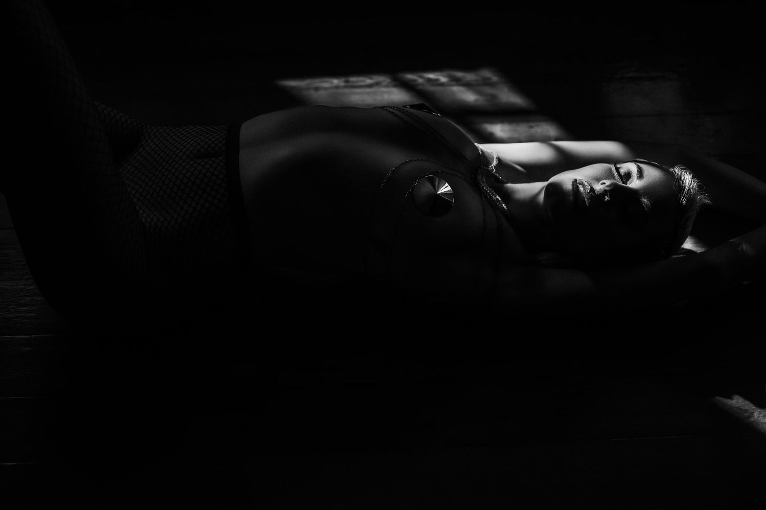 Black and white photo of a person lying on the floor in dramatic shadow and light contrast. dark boudoir photography new orleans
