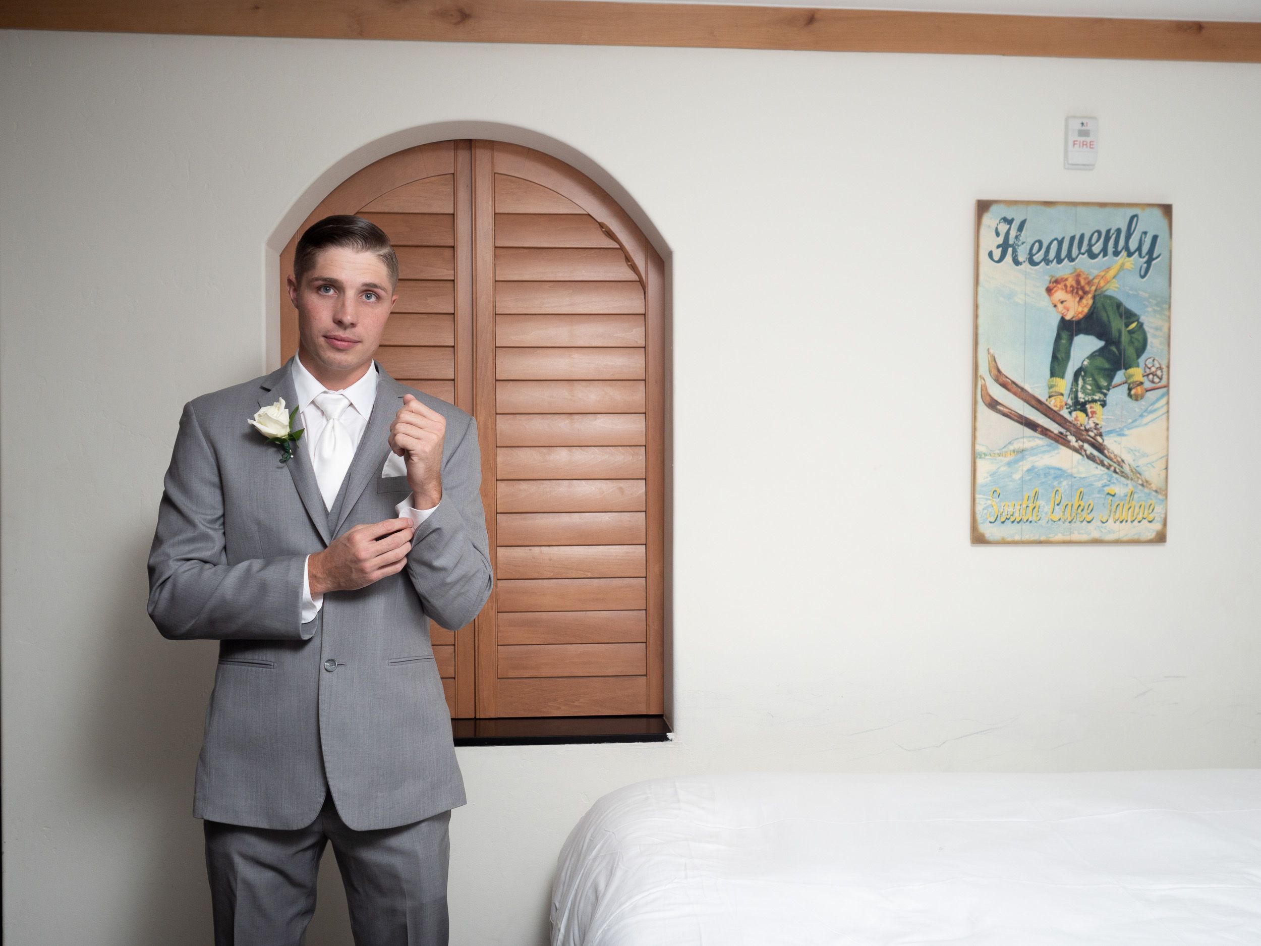 Groom in gray suit adjusting cufflinks in a room with a Heavenly ski resort vintage poster on the wall.