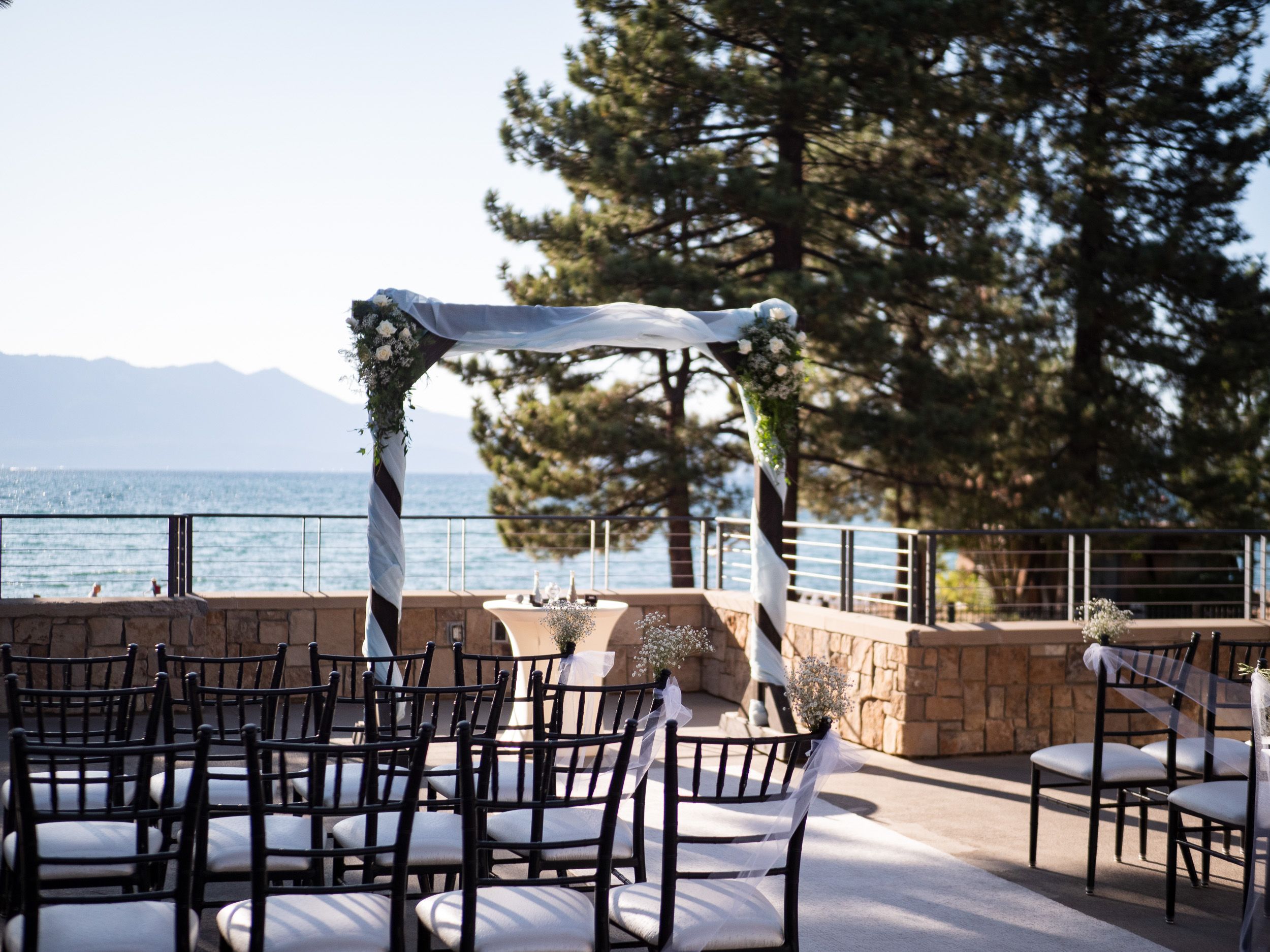 Elegant outdoor wedding ceremony setup with floral arch, chiavari chairs, and stunning lake and mountain views.