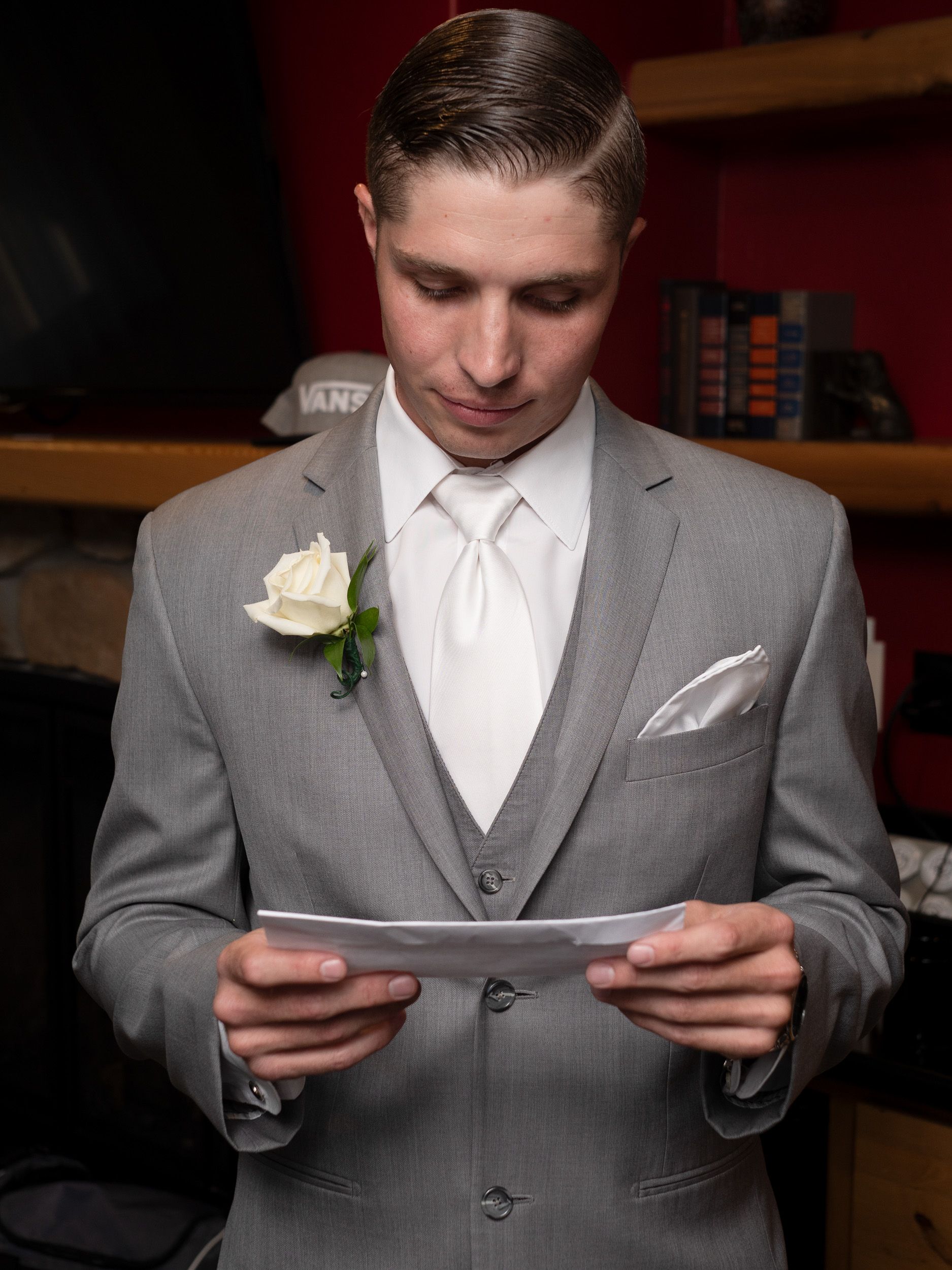 Groom in gray suit with white rose boutonniere reads a letter before his wedding ceremony.