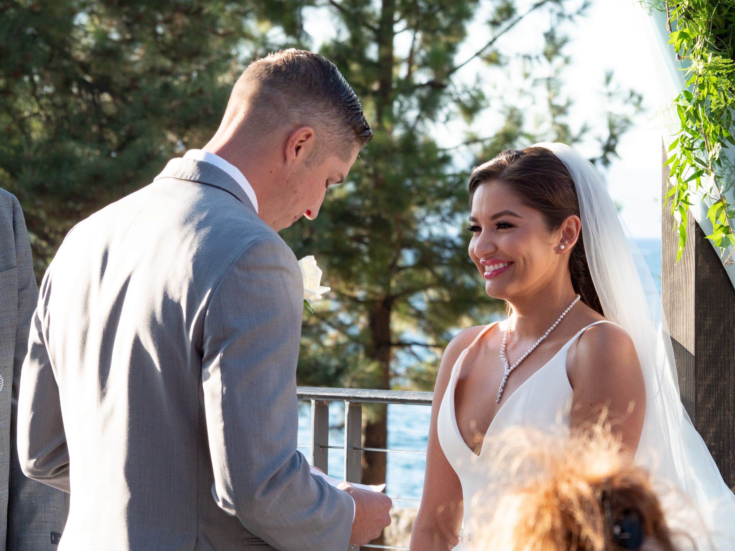 Bride and groom exchanging vows outdoors at a wedding ceremony with trees in the background.