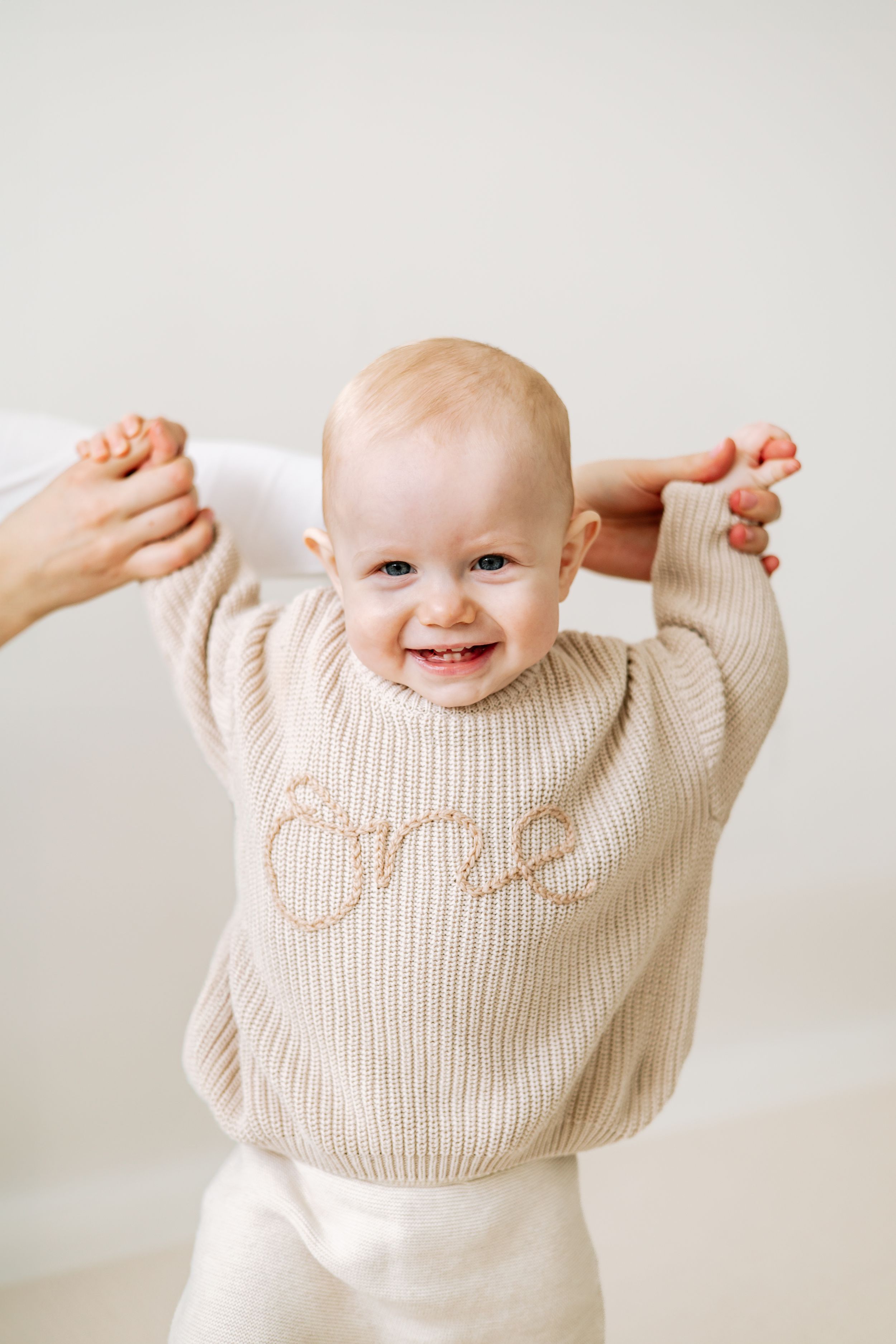 Smiling baby wearing a beige knit sweater with 'one' embroidered, celebrating their first birthday photography Nottingham