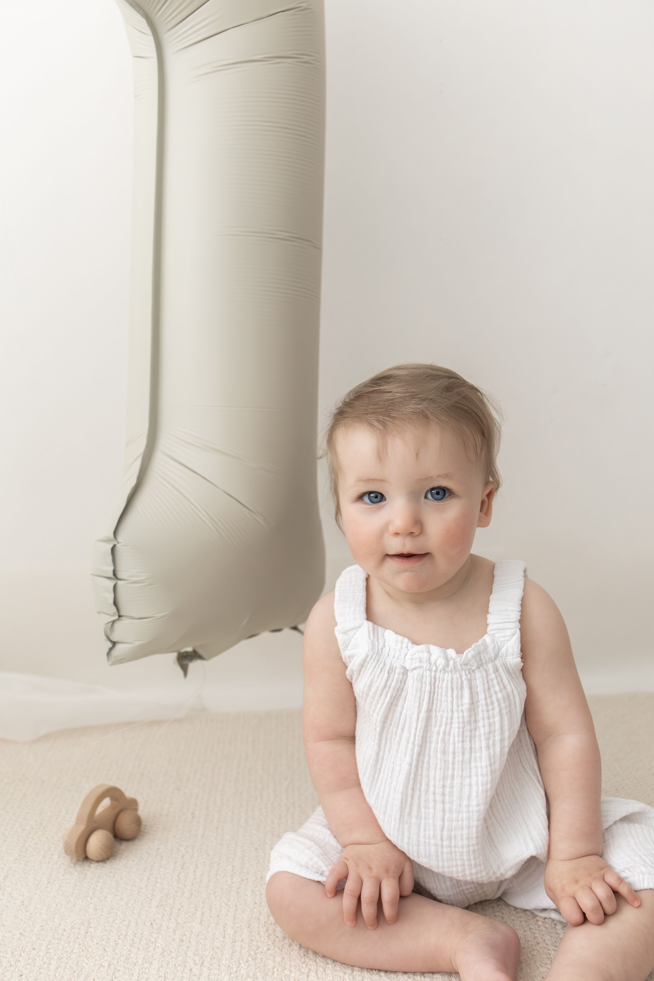 Baby birthday photoshoot Nottingham Baby in white romper sitting on floor beside a number 1 balloon, celebrating their first birthday.