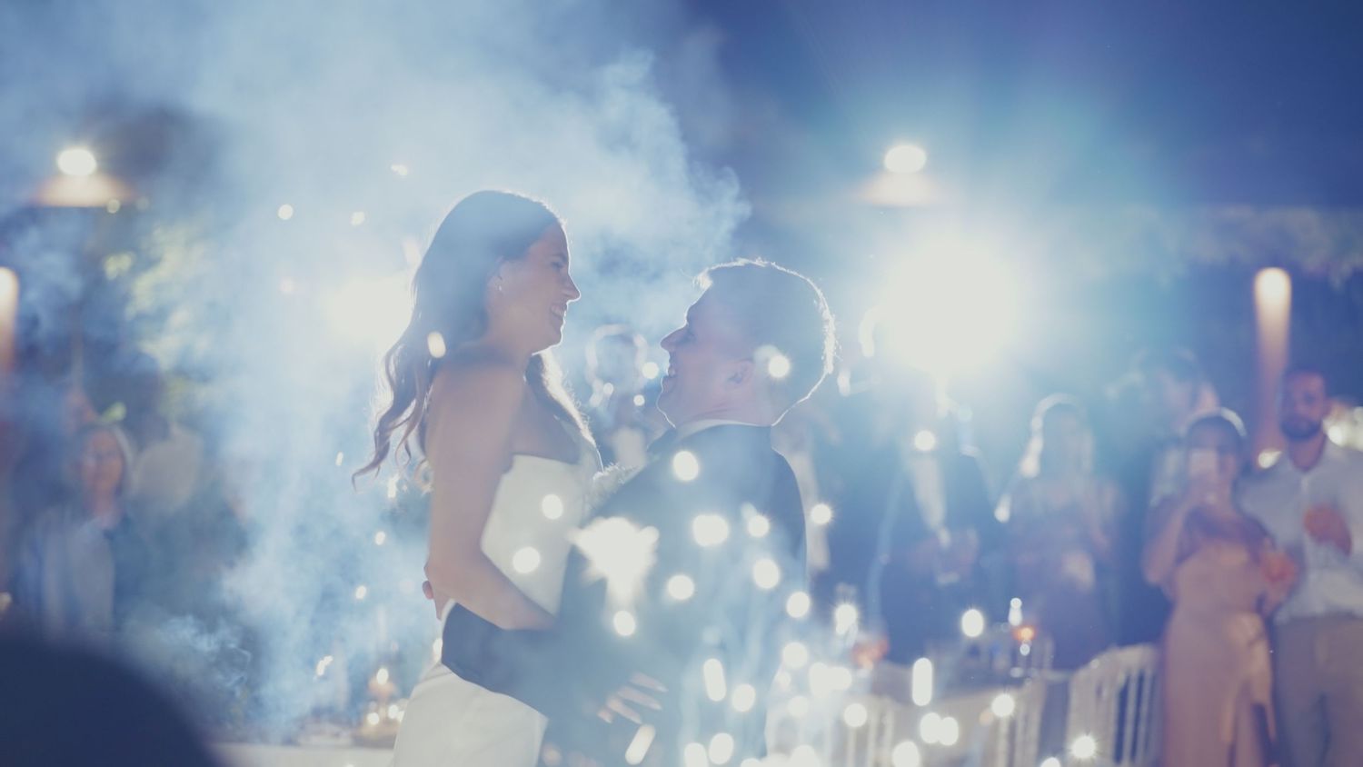 Couple sharing their first dance at a romantic wedding reception with sparkling lights and guests in the background.