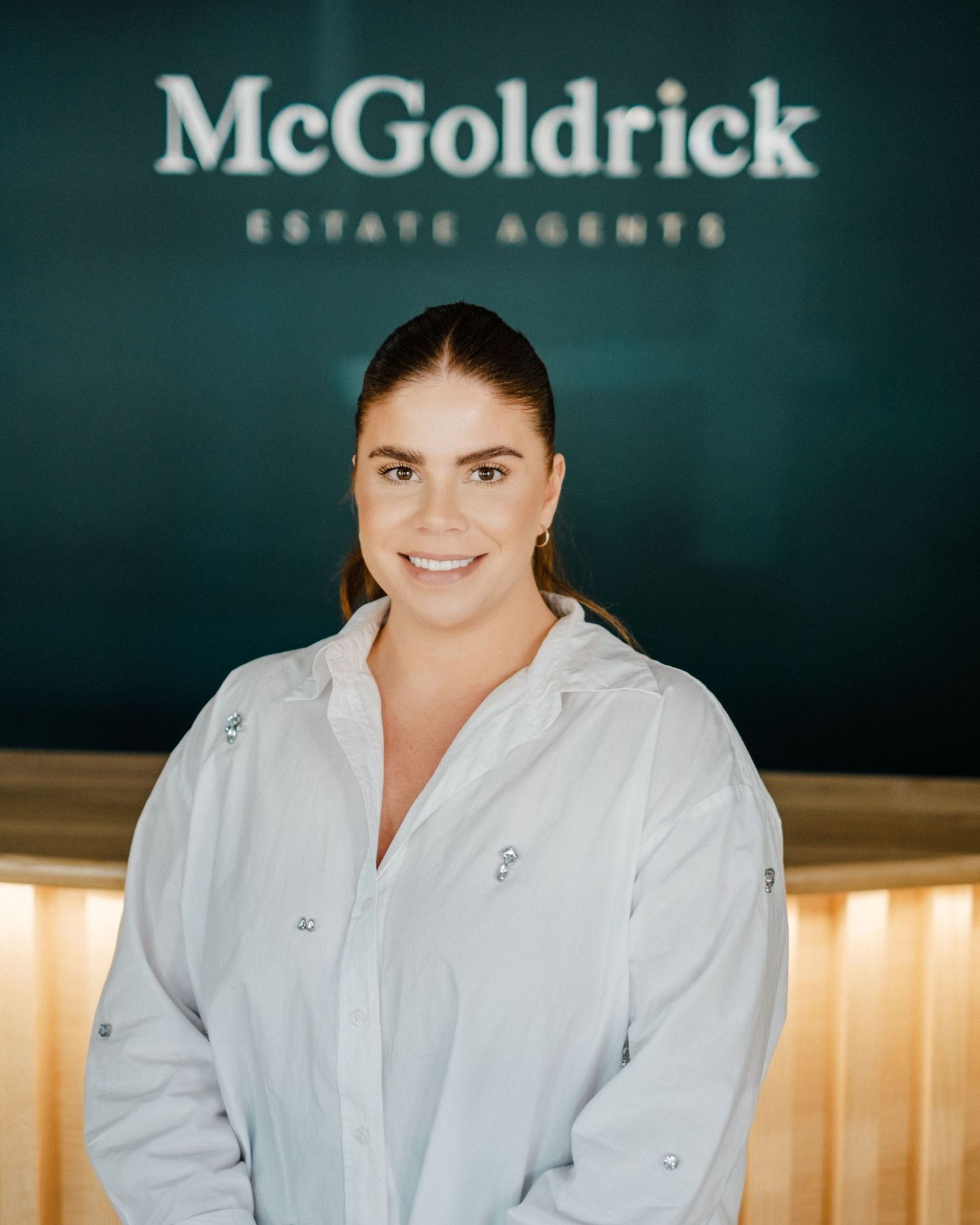 Woman smiling in front of McGoldrick Estate Agents sign in a modern office reception area.
