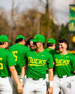 Oregon Ducks baseball players in green uniforms celebrate together on the field during a sunny game day.