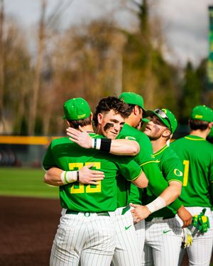 Oregon Ducks baseball players in green uniforms celebrate with hugs on the field during a college baseball game.