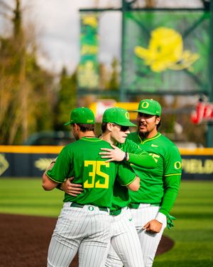 Oregon Ducks baseball players in green uniforms huddle together on the field during a game.