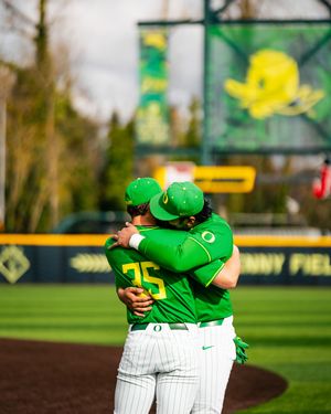 Two Oregon Ducks baseball players in green uniforms share a hug on the field at PK Park.