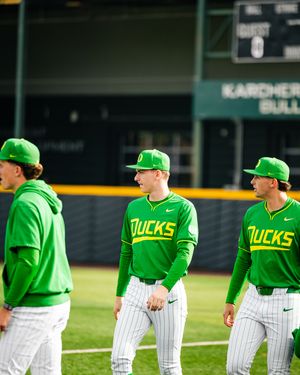 Oregon Ducks baseball players in green uniforms and caps warming up on the field before a game.