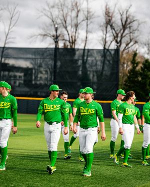 Oregon Ducks baseball players in bright green uniforms walk across the field during a cloudy day practice session.