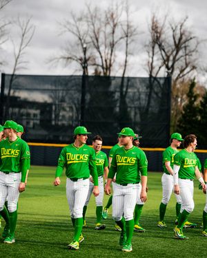 Oregon Ducks baseball players in green uniforms walk across the field during a pre-game warm-up session.