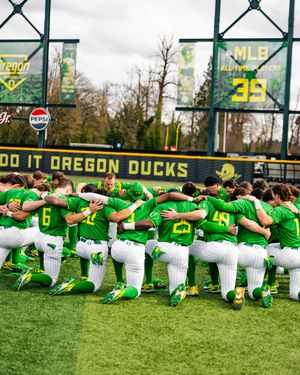 Oregon Ducks baseball team huddles together on the field in green uniforms at their home stadium.