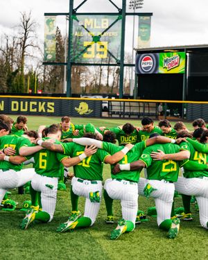 Oregon Ducks baseball team huddles together on the field in bright green uniforms during a pre-game gathering.