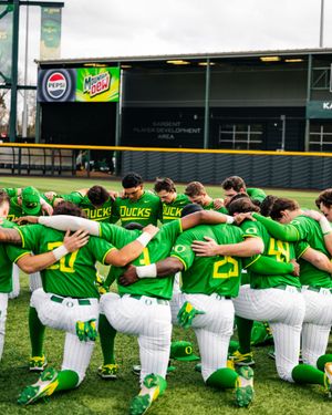 Oregon Ducks baseball team huddles together on the field in bright green uniforms during a pre-game team meeting.