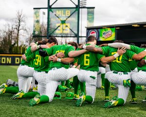 Oregon Ducks baseball team huddles together on one knee in green uniforms at PK Park before a game.