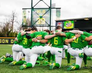 Oregon Ducks baseball team huddles on field in green uniforms, kneeling together before a game at their home stadium.
