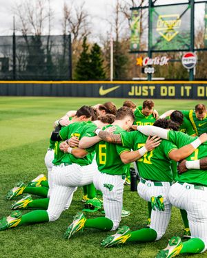 Oregon Ducks baseball team huddles together on the field in green and white uniforms at a Nike-sponsored stadium.