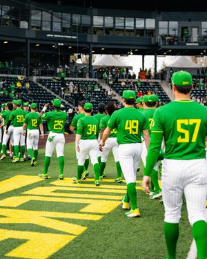 Oregon Ducks baseball team in bright green uniforms lining up on field at modern stadium.
