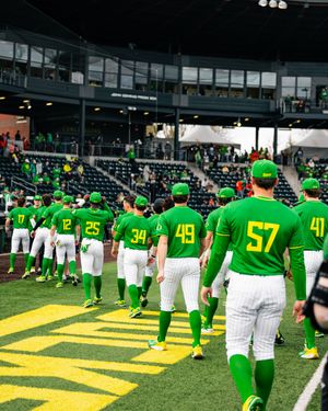 Oregon Ducks baseball team in green uniforms walking onto the field at a packed stadium during a game day.