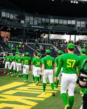 Oregon Ducks baseball team in green uniforms walking onto the field at a packed stadium during a game day.