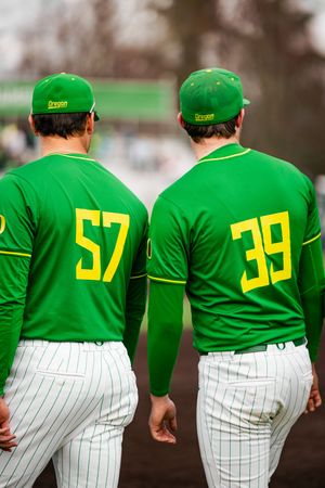 Two Oregon Ducks baseball players wearing green jerseys numbered 57 and 39 walk together on the field.