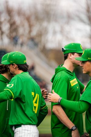 Oregon Ducks baseball players in green uniforms and caps huddle together on the field during a game.