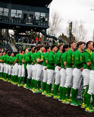 Oregon Ducks baseball team in green uniforms lined up on field during national anthem ceremony.