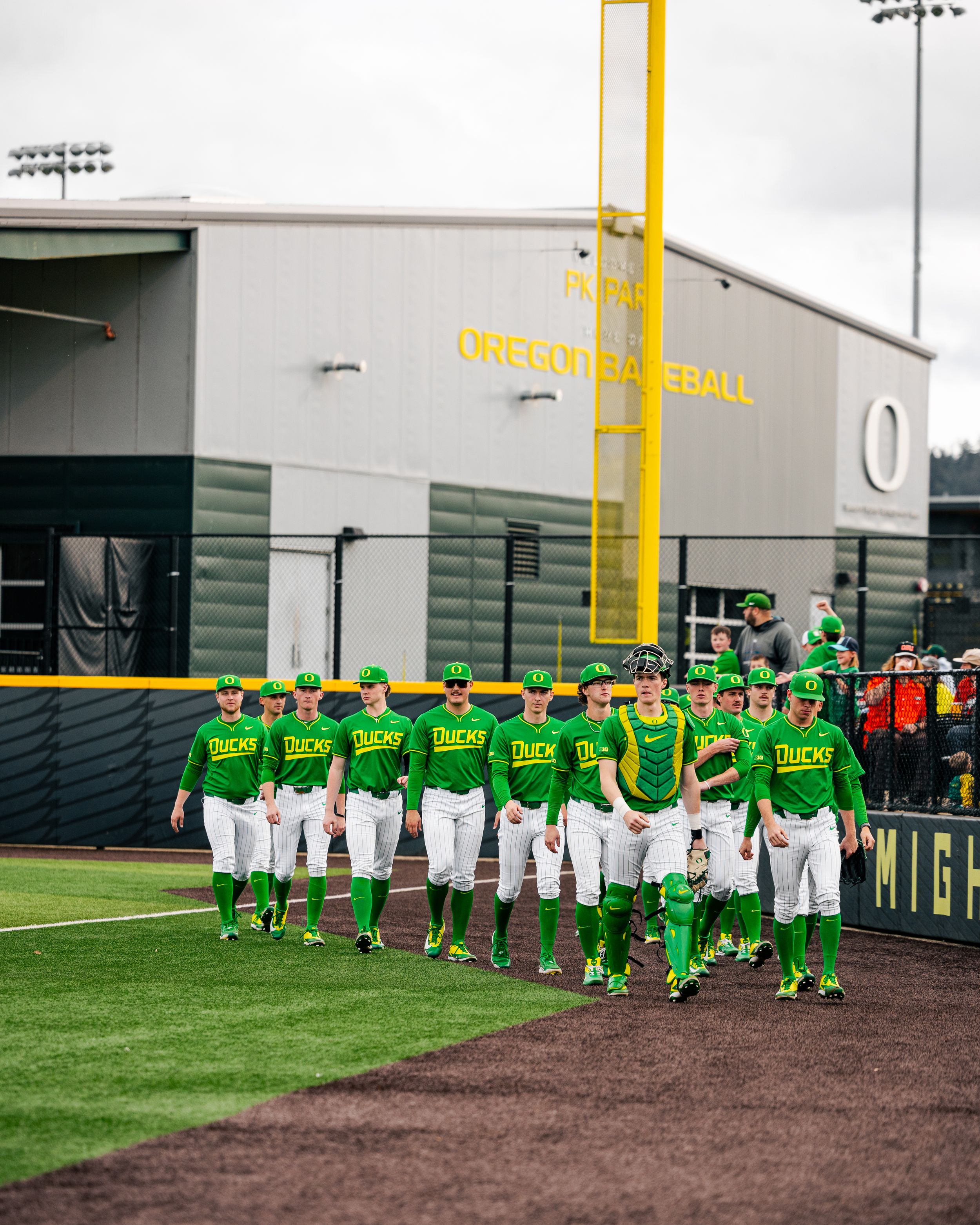 Oregon Ducks baseball team in green uniforms lined up on field outside PK Park stadium during a game day.