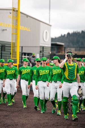Oregon Ducks baseball team in green uniforms walking on field at Oregon Baseball stadium.