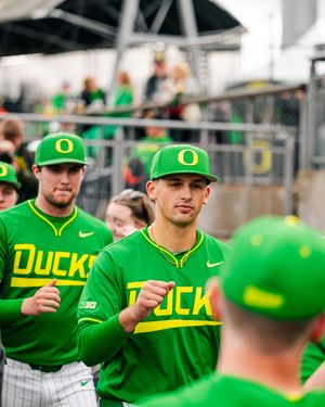 Oregon Ducks baseball players in bright green Nike uniforms walk through the dugout during a game.