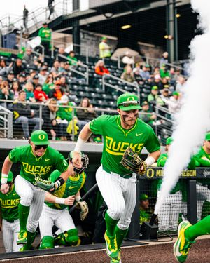 Oregon Ducks baseball players run onto the field in bright green uniforms during an exciting game entrance with smoke effects.