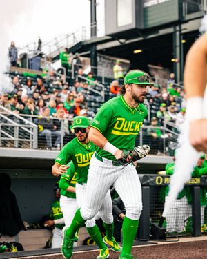 Oregon Ducks baseball players in bright green uniforms running onto the field at a packed stadium during a game.