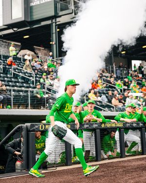 Oregon Ducks baseball player in green uniform runs onto field amid smoke during an exciting game day entrance at packed stadium.