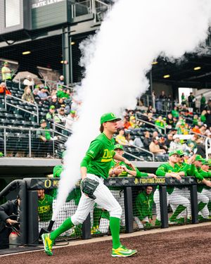 Oregon Ducks baseball player runs onto field through smoke during pregame introductions at packed stadium.