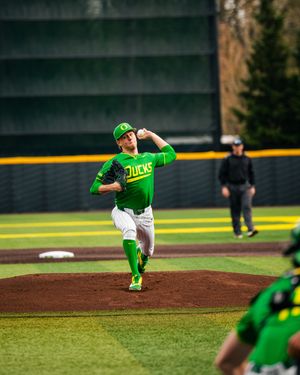 Oregon Ducks baseball pitcher in green uniform mid-windup on the mound during a college baseball game.