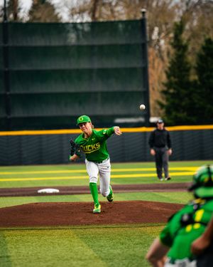 Oregon Ducks pitcher in green uniform delivers a pitch during a college baseball game on a dirt mound.